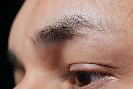 Professional barber doing threading procedure and correcting shape of eyebrows to young male client with tweezer in barber shop. Barber at work. Brow care concept. Plucking brows.の写真素材