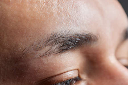 Professional barber doing threading procedure and correcting shape of eyebrows to young male client with tweezer in barber shop. Barber at work. Brow care concept. Plucking brows.の写真素材