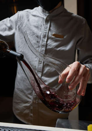 Sommelier man pours red wine into decanter for aeration of taste and aroma.