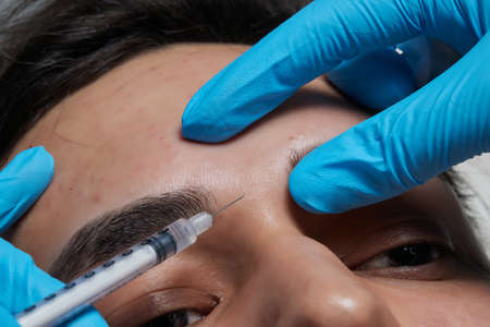 Mens cosmetology. Beautician injects a botulinum toxin into a mans forehead to relax the muscles....