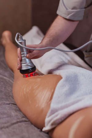 Hardware figure correction. Machine cosmetology. Beautiful woman having cavitation, procedure removing cellulite on her buttocks.の写真素材