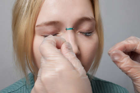 Nose Bridge Piercing Professional holding the jewel of piercing day just before screw the ball.の写真素材