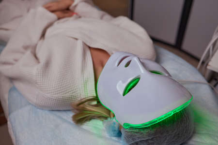 LED light anti-aging mask for facial skin care in a spa slow motion. A woman lies on a couch in a special mask. Modern technologies of beauty and health.の写真素材