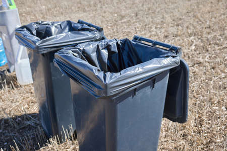 Trash bin on a field with garden weeds to be cleaned up.