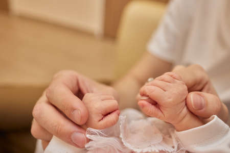 Mother uses her hand to hold her babys tiny hand to make him feeling her love, warm and secure.