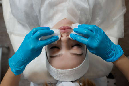 Mirthful young woman lying in a shower cap and hands in rubber gloves cleaning her skin with cotton...