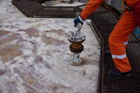 Young offshore engineer sounding fuel oil cargo tank on cargo deck on supply vessel in harbor.