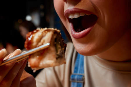 Cropped young woman 20s wear casual clothes hold in hand makizushi sushi roll served on plate traditional japanese food.の写真素材