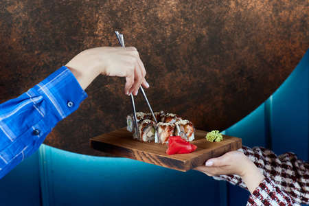Cropped young woman 20s wear casual clothes hold in hand makizushi sushi roll served on plate traditional japanese food.の写真素材