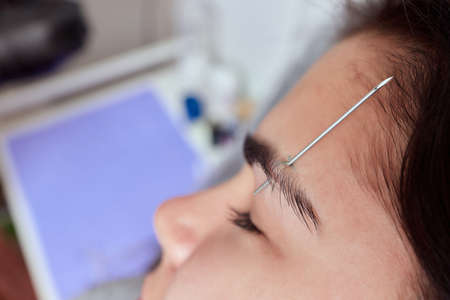 Professional placing the jewel of piercing on the temple on the head with ball. Tragus type.の写真素材