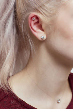 piercings on an ear. Conch and helix piercings close up. Professional holding the jewel.