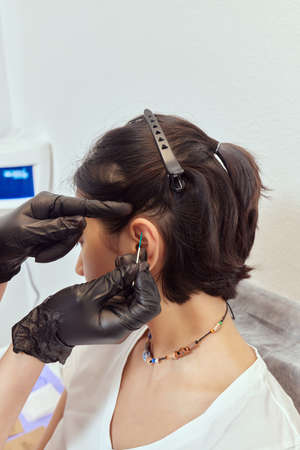 piercings on an ear. Conch and helix piercings close up. Professional holding the jewel.