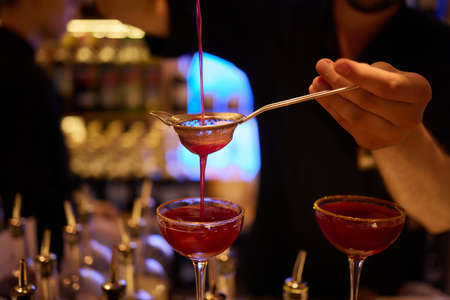 Bartender pouring strong alcoholic drink into small glasses on bar, shots.