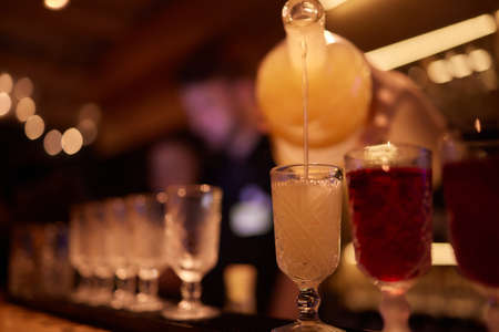 Bartender pouring strong alcoholic drink into small glasses on bar, shots.