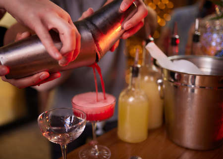 Bartender pouring strong alcoholic drink into small glasses on bar, shots.
