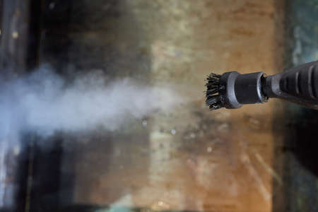 Experienced worker in rubber gloves steam-cleaning kitchen equipment.の写真素材