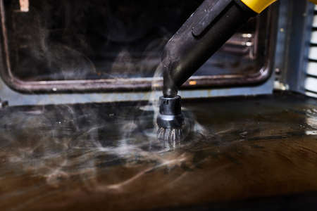 Experienced worker in rubber gloves steam-cleaning kitchen equipment.の写真素材