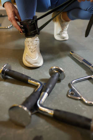 Young woman in trainers buckling a leather strap to her ankle as she sits on the floor of a gym in a health and fitness concept.の写真素材