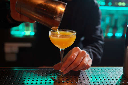 Barman in shirt and apron making an alcoholic drink with ice in a cocktail glass.の写真素材