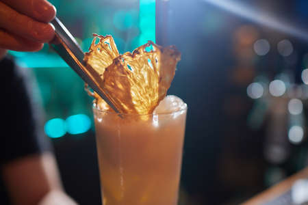 Barman in shirt and apron making an alcoholic drink with ice in a cocktail glass.の写真素材