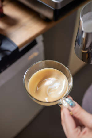 Top view shot of professional barista pouring milk from jar in to a cup of coffee, coffee being prepared by a barista. Focus on hands holding cup of coffee.の写真素材