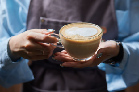 Top view shot of professional barista pouring milk from jar in to a cup of coffee, coffee being prepared by a barista. Focus on hands holding cup of coffee.の写真素材