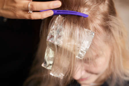 Hair stylist makes bouffant using comb on thin strands. Shatush technique for hair lightening.の写真素材