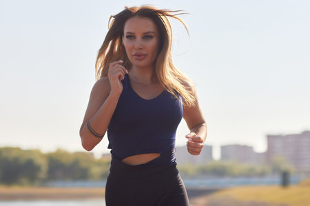Athletic slim woman on a sunny day runs along the embankment or park.