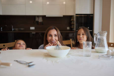 Cute little girl and her beautiful mom in aprons are playing and laughing while kneading the dough...