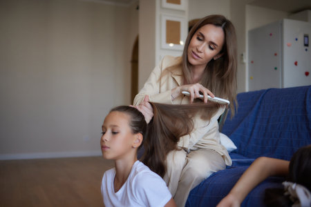 Close up photo of happy smiling schoolgirl with curly long dark hair and her beautiful mum who is brushing her hair.の写真素材