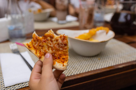 Asian child holding slice of delicious hot pizza over table.