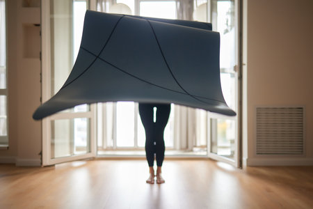 Close-up of an attractive young woman laying out a blue yoga or fitness mat before exercising in the studio. Healthy lifestyle.の写真素材
