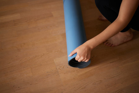 Close-up of an attractive young woman laying out a blue yoga or fitness mat before exercising in the studio. Healthy lifestyle.の写真素材