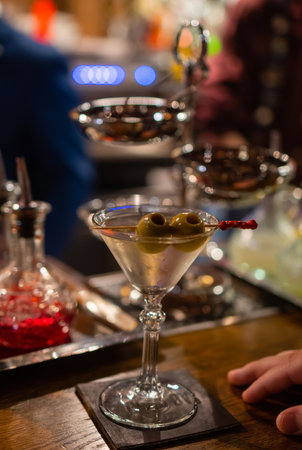 martini with green olives on a table in bar.