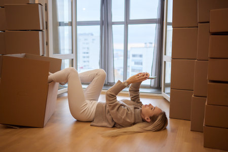 Young woman moving new place and repair concept - happy young woman with many cardboard boxes sitting on floor at home.の写真素材