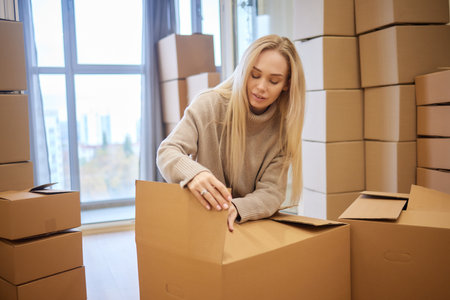 Young woman moving new place and repair concept - happy young woman with many cardboard boxes sitting on floor at home.の写真素材