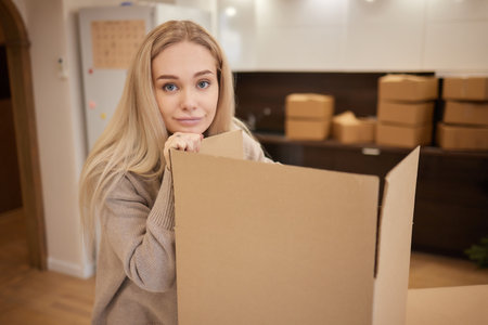 Caucasian girl taping boxes for moving in new apartment.