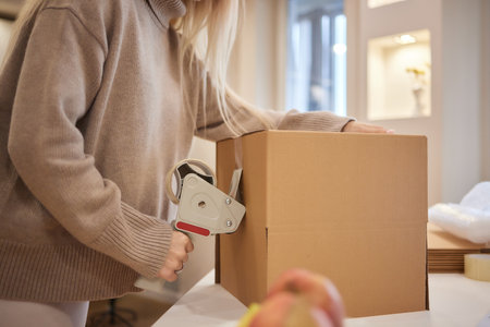 Young business woman taping up a cardboard box in the office, relocation and new business concept.