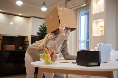 Young entrepreneur is holding cardboard boxes and place it on her head after successfully in sale products while sitting on comfortable the couch and working in living room at home office.の写真素材
