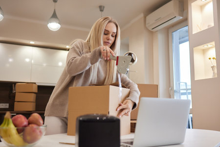 Young business woman taping up a cardboard box in the office, relocation and new business concept.の写真素材