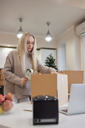 Young business woman taping up a cardboard box in the office, relocation and new business concept.