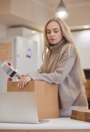Young business woman taping up a cardboard box in the office, relocation and new business concept.