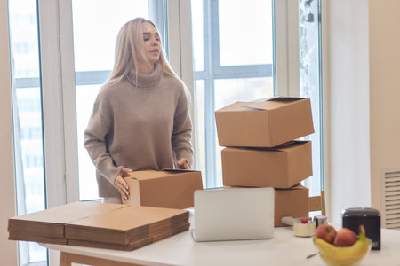 Happy homeowner, renter girl using laptop at pile of stacked boxes, ordering delivery, shipping, transportation service for moving out, looking away, dreaming of new apartment, smiling.の写真素材