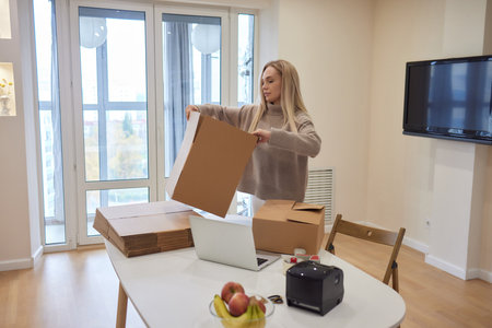 Happy homeowner, renter girl using laptop at pile of stacked boxes, ordering delivery, shipping,...