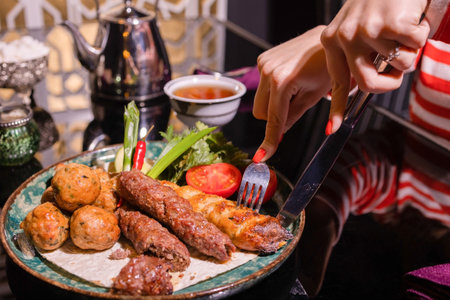 Woman eating barbecue in a cafe. Female hands close-up holding a fork with a piece of barbecue.