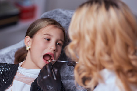 Caucasian young child girl sitting in medical chair while dentist fixing teeth at dental clinic...