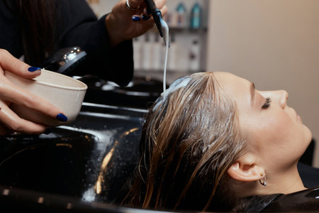 Hairdresser in beauty salon washes his client hair, before procedure of applying natural restoring ingredients and vitamins to hair and haircut.の写真素材