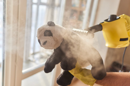 cleaning childs fliffy toys with steam, hands in blue glove hold steam genetator andbrush with steam...