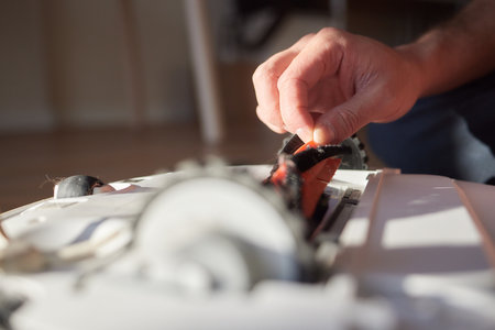 A hand in a blue glove holds a clump of hair and pet hair removed from the brush of a robot vacuum...