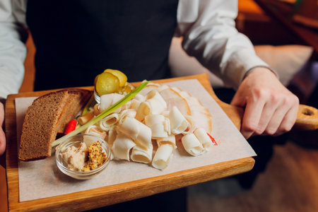 In a beautiful restaurant, a waiter brings a ready-made dish for a young guy man in a suit, on a tray of oak lard with garlic. Concept from: Garlic, lard, New dish, Unusual serving, Fresh, Vegetable.の写真素材